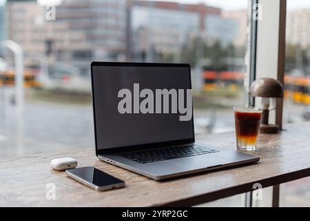 Moderner Laptop mit Smartphone und Espresso Tonic Kaffee auf Holztisch im Büro im urbanen Hintergrund. Workflow, Konzept. Laptop-Modell, kostenloser Whirlpool Stockfoto