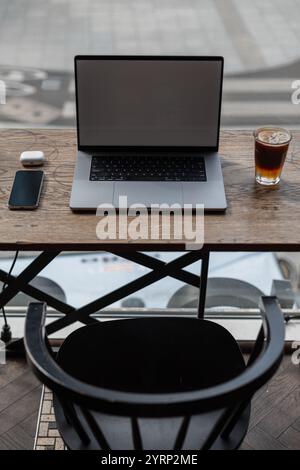 Laptop mit Smartphone, Kopfhörern und köstlichem aromatischem Espresso Tonic Kaffee auf Holztisch mit Stuhl im Café auf urbanem Hintergrund. Am Arbeitsplatz und Stockfoto