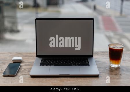 Laptop-Modell mit Smartphone, Kaffee Espresso Tonic und Kopfhörern steht auf Vintage Holztisch auf urbanem Hintergrund im Büro. Kreative Idee und Arbeitsauftrag Stockfoto