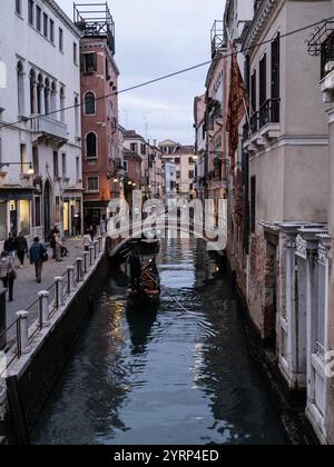 Touristen auf einer Gondelfahrt entlang eines Wasserkanals auf den Straßen von Venedig, Italien Stockfoto