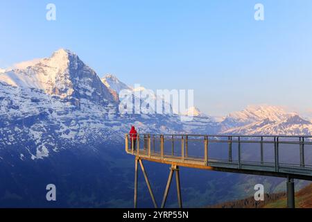 Ein Besucher in roter Jacke steht auf der Aussichtsplattform Cliff Walk am ersten, Gwindelwald in den Morgenstunden gegen die Schneeberge Stockfoto