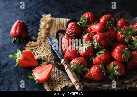 Frische Erdbeeren auf einem Vintage-Teller über Leinen auf dem Tisch vor dunklem Hintergrund - dunkle und stimmungsvolle Fotografie Stockfoto