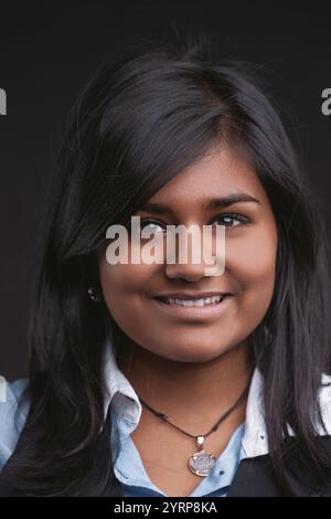 Porträt einer jungen indischen Geschäftsfrau, die selbstbewusst in die Kamera lächelt und Professionalität und Zugänglichkeit vor einem einfachen schwarzen Backdro ausstrahlt Stockfoto