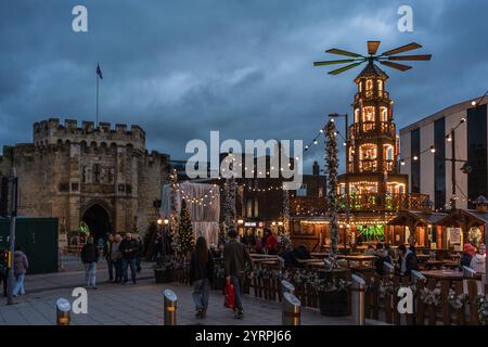 Southampton, Großbritannien. Dezember 2024. An einem kalten Wintertag, an dem der jährliche traditionelle deutsche Weihnachtsmarkt stattfindet, spazieren die Menschen entlang des Southampton Precinct. Hier ist die beleuchtete Weihnachtspyramide mit dem historischen Southampton Bargate im Hintergrund abgebildet. Stockfoto