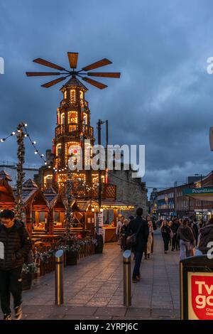 Southampton, Großbritannien. Dezember 2024. An einem kalten Wintertag, an dem der jährliche traditionelle deutsche Weihnachtsmarkt stattfindet, spazieren die Menschen entlang des Southampton Precinct. Hier ist die beleuchtete Weihnachtspyramide mit dem historischen Southampton Bargate im Hintergrund abgebildet. Stockfoto