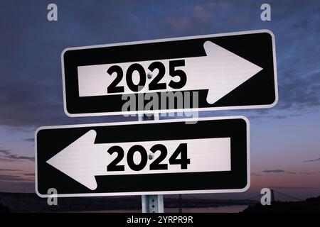 Straßenschilder zeigen den Weg zum neuen Jahr 2025 und zum alten Jahr 2024 am Abend, kreative Idee. Wählen Sie einen neuen Weg zum 2025-jährigen Konzept. Ändern für Stockfoto