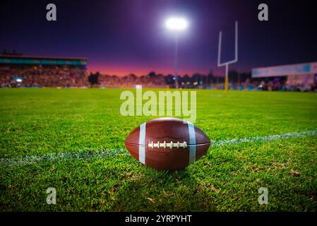 American Football Scene unter Stadionlichtern mit einem American Football Ball auf einem üppigen grünen Feld bei Sonnenuntergang, der mit Goalp eine ruhige Abenddämmerung einnimmt Stockfoto