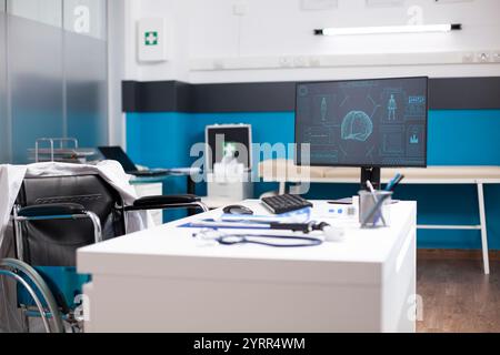 Unbesetztes Gesundheitsbüro mit Desktop-Monitor, der Gehirn- und Körperscanddaten für neurologische Untersuchungen anzeigt. Ein organisierter, rollstuhlgerechter Schreibtisch mit Diagnosegeräten ist bereit für die Patientenanalyse. Stockfoto