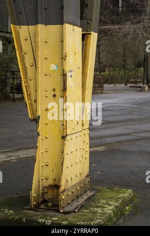 Nahaufnahme einer verwitterten gelben Metallsäule mit Nieten und Rostspuren, die eine größere Industriestruktur unterstützen Stockfoto