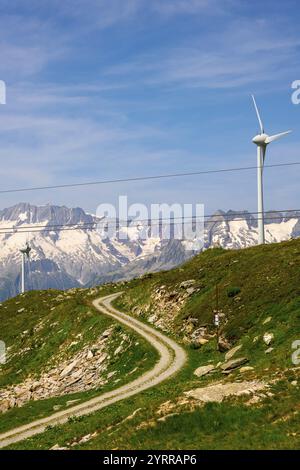 Windturbine und Berg mit Gletscher und Seilbahn und blauem Himmel und Wolken an einem sonnigen Sommertag in Andermatt, URI, Schweiz. Stockfoto