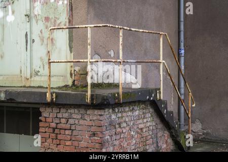 Rostiges Geländer und Treppen führen zu einer verwitterten grünen Tür in einer urbanen Umgebung, die Anzeichen von Verfall und Vernachlässigung zeigt Stockfoto