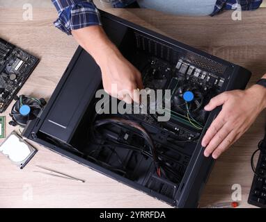 Mann, der einen neuen Computer an einem Holztisch zusammenbaut, Draufsicht Stockfoto