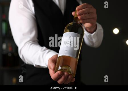 Professioneller Sommelier hält eine Flasche Weißwein drinnen, Nahaufnahme Stockfoto