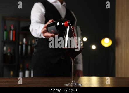 Professioneller Sommelier, der Rotwein in Glas an einem Holztisch drinnen in der Nähe gießt Stockfoto