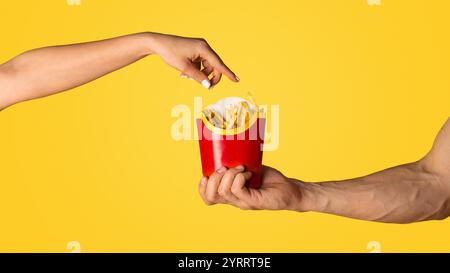 KHARKIV, UKRAINE - 4. APRIL 2020: Mann und Frau mit einer Packung pommes Frites von McDonald's auf orangefarbenem Hintergrund Stockfoto