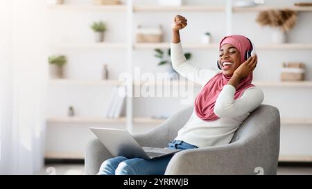 Überglücklich Schwarze Islamische Dame In Kabellosen Kopfhörern Musik Online Auf Laptop Hören Stockfoto