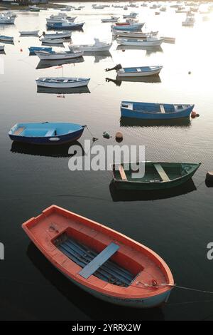 Farbenfrohe Fischerboote, die bei Sonnenuntergang friedlich im ruhigen Hafenwasser schwimmen Stockfoto