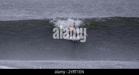 Gilgo Beach, New York USA - 30. August 2023: Ein Surfer fängt eine Welle am Strand, während der Himmel bewölkt und das Wasser abgehackt ist. Stockfoto
