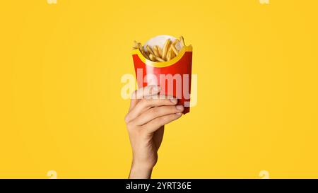 KHARKIV, UKRAINE - 4. APRIL 2020: Millennial guy zeigt kleine Packung pommes aus McDonald's auf orangefarbenem Hintergrund Stockfoto