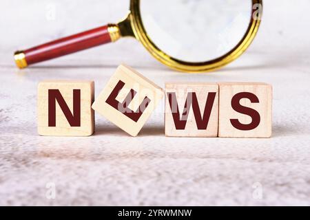 Kommunikation über aktuelle Ereignisse. NACHRICHTEN geschrieben auf Holzwürfeln mit einer Lupe im Hintergrund. Stockfoto