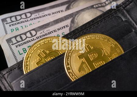 Bitcoin und 100 Dollar sichtbar in einer offenen schwarzen Ledergeldbörse Stockfoto