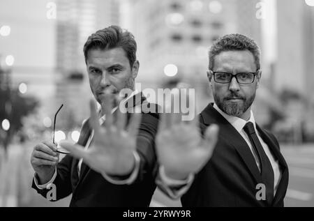 Krise, Risiko. Zwei gutaussehende Geschäftsleute im Anzug hören auf mit der Hand zu singen. Warnausdruck mit negativer und ernsthafter Geste im Gesicht. Halt die Hand an Stockfoto