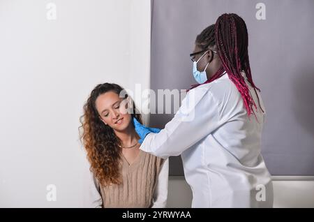 Ärztin untersucht die Drüsen des Patienten in einer Arztpraxis, trägt Maske und Handschuhe aus Sicherheitsgründen Stockfoto