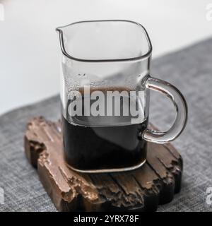 Ein eleganter Glaskrug mit einem dunklen Getränk, das auf einem Holzsockel schön ausgestellt ist Stockfoto