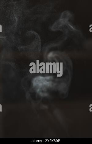 Ätherische und fesselnde Rauchmuster tauchen anmutig vor einem dunklen, reichen Hintergrund auf Stockfoto