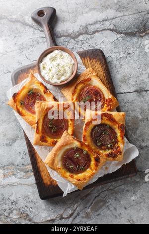 Puff Mini Torten mit karamelisierten roten Zwiebeln in Nahaufnahme auf einem Holzbrett auf einem Tisch. Vertikale Draufsicht von oben Stockfoto