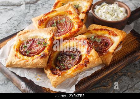 Puff Mini Torten mit karamelisierten roten Zwiebeln in Nahaufnahme auf einem Holzbrett auf einem Tisch. Horizontal Stockfoto