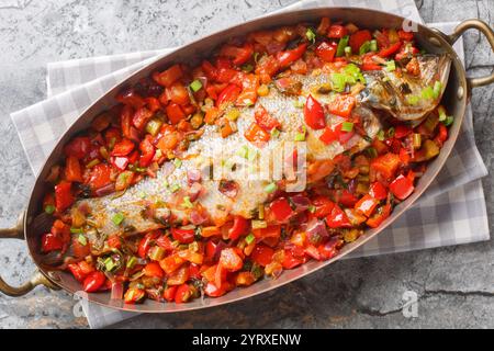 Ganzer Wolfsbarsch, gebacken mit saisonalem Gemüse wie Pfeffer, Tomaten, Zwiebeln, Sellerie und Knoblauch in einer Pfanne auf dem Tisch. Horizontal oben V Stockfoto