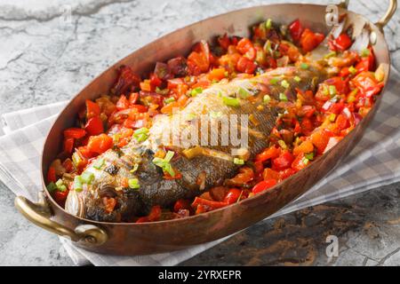 Ganzer Wolfsbarsch, gebacken mit saisonalem Gemüse wie Pfeffer, Tomaten, Zwiebeln, Sellerie und Knoblauch in einer Pfanne auf dem Tisch. Horizontal Stockfoto