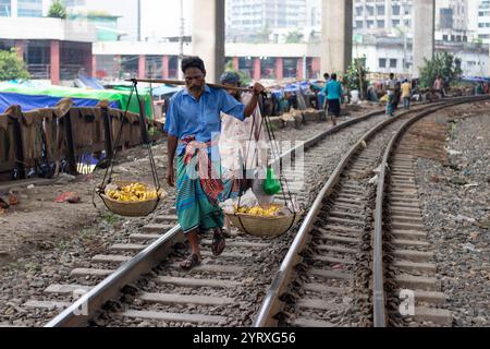 Dhaka, Dhaka, Bangladesch. Dezember 2024. Das Leben entlang der Bahngleise im Kawran Basar in Dhaka ist voller Aktivität und Herausforderungen. Händler transportieren Obst, Gemüse und Hühner über die Gleise, um den Markt zu erreichen, und bewegen sich vorsichtig zwischen vorbeifahrenden Zügen. Pendler nutzen die Strecken auch als Abkürzung und gehen oft Risiken ein, um Zeit zu sparen. Viele Menschen leben neben den Gleisen und verbringen ihre Tage in der Nähe der ständigen Bewegung der Züge. Trotz der Gefahren ist diese Gegend ein wichtiger Bestandteil des täglichen Lebens der Stadt. (Kreditbild: © Joy Saha/ZUMA Press Wire) NUR REDAKTIONELLE VERWENDUNG! Nicht für Commercia Stockfoto