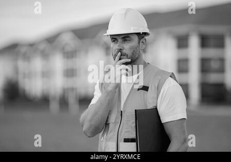 Baumeister-Denken. Bauarbeiter im Helm bauen ein neues Haus. Ingenieure arbeiten in Baukleidung und Schutzhelm. Foreman Porträt im Freien. 40s Arbeiter Stockfoto