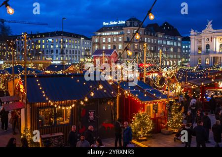 3-12-2024 Zürich, Schweiz. Besucher besuchen Pop-up-Shops auf dem Weihnachtsmarkt am Sechselautenplatz. Blaue Stunde am späten Abend, Weihnachtsbeleuchtung. Stockfoto