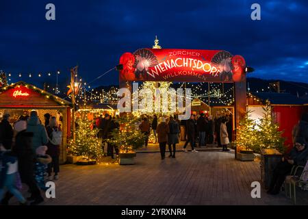 3-12-2024 Zürich, Schweiz. Besucher besuchen Pop-up-Shops auf dem Weihnachtsmarkt am Sechselautenplatz. Blaue Stunde am späten Abend, Weihnachtsbeleuchtung. Stockfoto