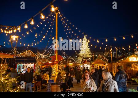 3-12-2024 Zürich, Schweiz. Besucher besuchen Pop-up-Shops auf dem Weihnachtsmarkt am Sechselautenplatz. Blaue Stunde am späten Abend, Weihnachtsbeleuchtung. Stockfoto