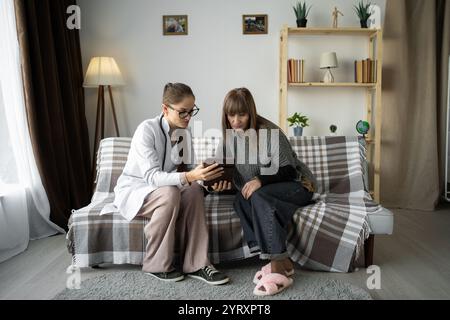 Hausärztin zeigt Testergebnisse auf Tablet-Computer bei Rentnerinnen während der Hausberatung. Stockfoto