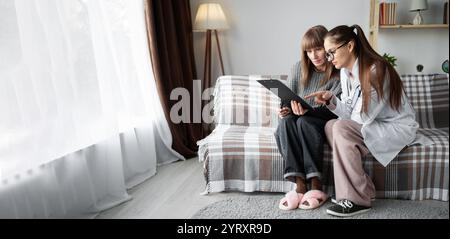 Weibliche Ärztin berät ältere Patienten zu Hause und gibt abschließende Diagnose und Behandlungsempfehlungen für Krankheit, die im Sitzen auf der Zwischenablage gelesen werden Stockfoto