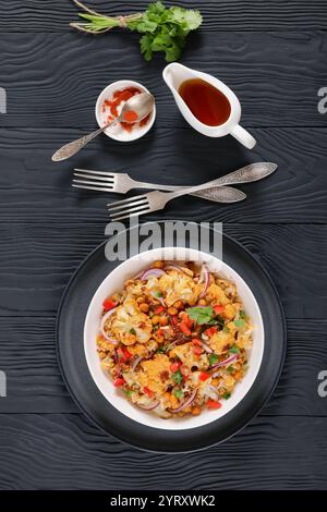 Gebratener Blumenkohl-Quinoa-Salat mit Walnüssen, rotem Pfeffer, Zwiebeln und Koriander in weißer Schüssel auf schwarzem Holztisch mit Gabeln, vertikale Ansicht, Stockfoto