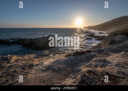 Die Sonne untergeht über dem Pazifik am Leo Carrillo State Beach und wirft goldenes Licht auf die felsige Küste und sanfte Wellen. Stockfoto