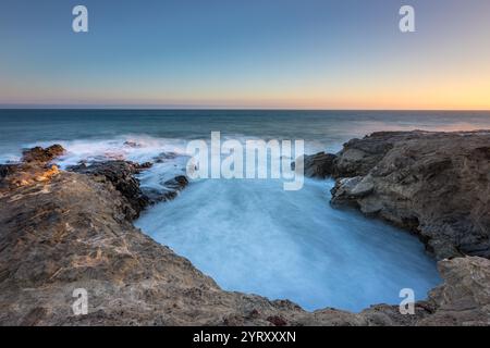 Wellen brechen am Leo Carrillo State Beach während des Sonnenuntergangs in Malibu, Kalifornien, gegen Felsformationen ab und bilden Schaum. Stockfoto