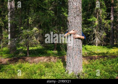 Ein junger Mann umarmt einen Baumstamm, umgeben von üppigen Wäldern, das Umweltbewusstsein und eine tiefe Verbindung mit der Natur symbolisiert Stockfoto