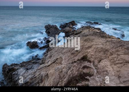 Die Wellen brechen in der Abenddämmerung am Leo Carrillo State Beach gegen die felsige Küste und zeigen die natürliche Schönheit von Malibu, Kalifornien. Stockfoto