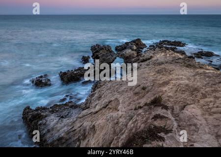 Am Leo Carrillo State Beach erheben sich zerklüftete Felsformationen aus dem Meer, während die Wellen während der Dämmerung sanft gegen die Küste krachen. Stockfoto