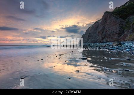 Leuchtende Farben bei Sonnenuntergang spiegeln sich auf dem ruhigen Wasser von Dana Cove wider, während die Wellen sanft an der Küste von Dana Point, Kalifornien, anschlagen. Stockfoto