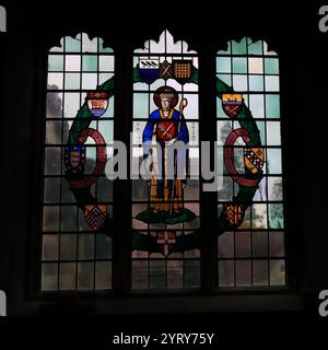 Romsey, Southampton, England. November 2024. Im Inneren der Romsey Abbey: Ein beleuchtetes dreifarbiges Buntglasfenster mit dem Heiligen Swithun. Stockfoto