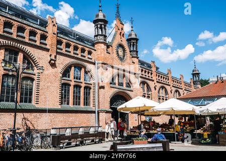 Historische Markthalle in Danzig mit roter Backsteinarchitektur und Outdoor-Produkten unter Sonnenschirmen. Lebhafte Marktplatzszene. Danzig, Polen - Mai Stockfoto