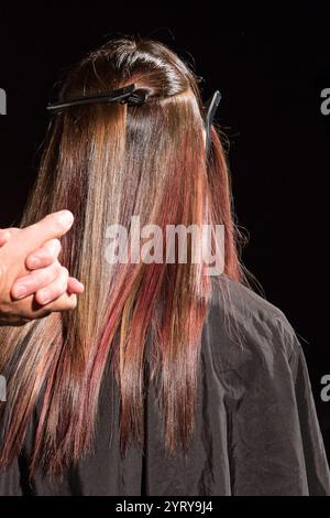 Friseur färbt Frauenhaare mit roter Färbung im professionellen Friseursalon mit schwarzem Hintergrund Stockfoto